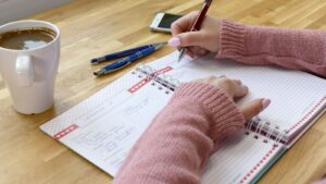 Persona planificando sus hábitos diarios en un cuaderno con un café